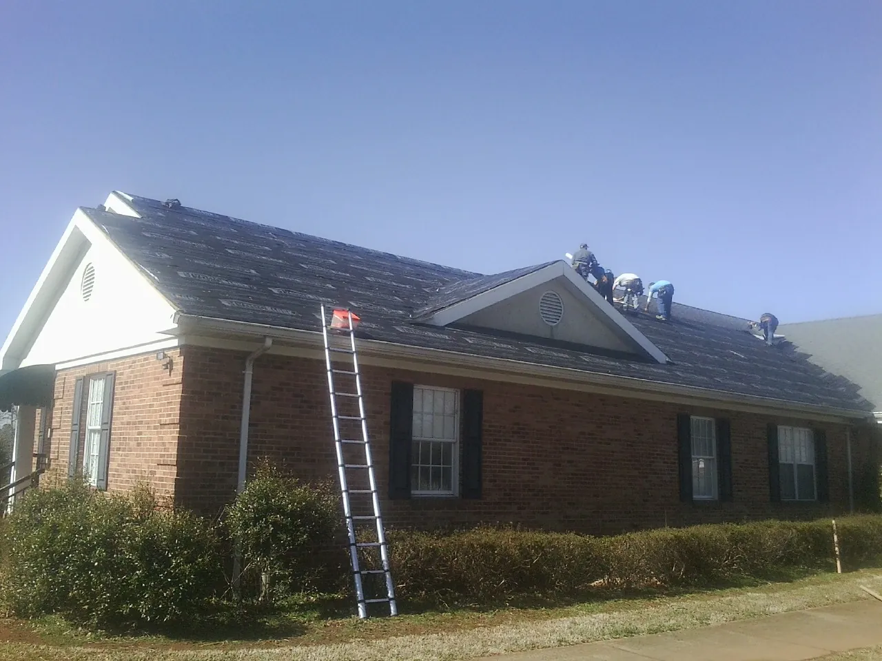 Crew tearing shingles off a brick ranch roof with a ladder set — Emergency Roof Repair work by our crew in Hampton
